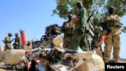 South Sudan army soldiers stand next to a destroyed motorcycle near Bor Airport, northwest of capital Juba, Dec. 25, 2013. 