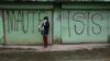 FILE - A person is seen using a mobile phone while passing a shuttered store front with "MAUTE-ISIS" graffiti, in Marawi city, southern Philippines, Oct. 20, 2017.